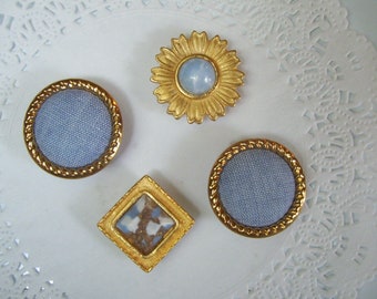 May include: Four gold-toned buttons with blue fabric centers. Two buttons have a round shape, one has a square shape, and one has a flower shape with a blue stone in the center.