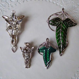 May include: Four silver and green leaf-shaped brooches. Two of the brooches are green with silver outlines, and two are silver with a leaf design.