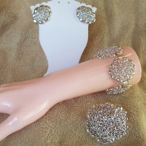 May include: A silver bracelet with a chain link design and a silver brooch with a similar design. The bracelet and brooch are on a brown fabric background.