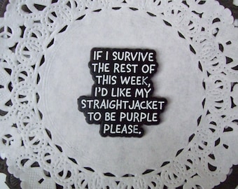 May include: A black and white rectangular pin with the text "IF I SURVIVE THE REST OF THIS WEEK, I'D LIKE MY STRAIGHTJACKET TO BE PURPLE PLEASE." The pin is on a white doily with a dark brown border.