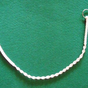 May include: A white braided cord necklace with silver clasps. The necklace is on a green surface.