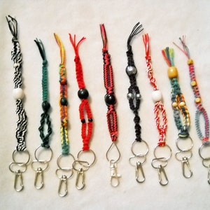 May include: Ten colorful keychains with different bead accents and metal key rings. The keychains are made of braided string in various colors, including red, black, white, green, blue, and yellow.