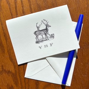 May include: A white card with a black and white illustration of two deer with antlers. The card has the initials "VSF" printed in black.