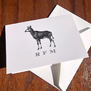 May include: A white card with a black and white illustration of an okapi, a type of African mammal. The card has the initials "RFM" printed in black below the illustration.