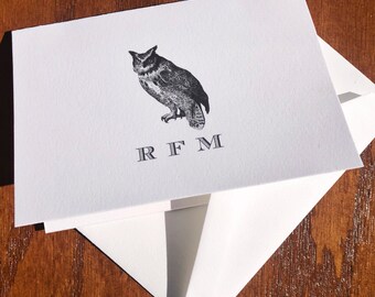 May include: A white card with a black and white illustration of an owl and the monogram "RFM" printed in black.