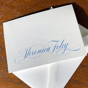 May include: A white card with a blue cursive script that reads "Veronica Foley".