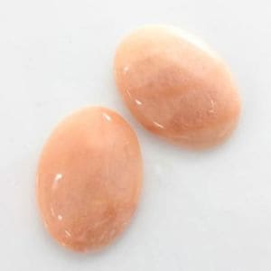 May include: Two oval-shaped, pale pink, smooth, polished stones. The stones have a pearlescent sheen.