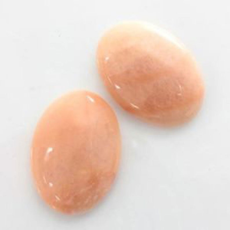 May include: Two oval-shaped, pale pink, smooth, polished stones. The stones have a pearlescent sheen.