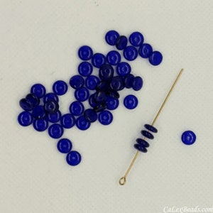 Puede incluir: Un montón de pequeñas cuentas redondas de vidrio azul cobalto, algunas de las cuales están enhebradas en un alambre dorado.