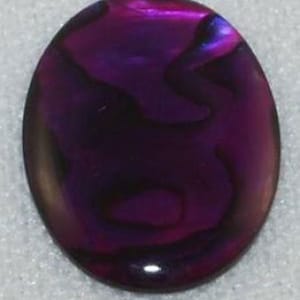 May include: A purple abalone shell cabochon with iridescent swirls. The shell is oval shaped and has a smooth, polished surface.