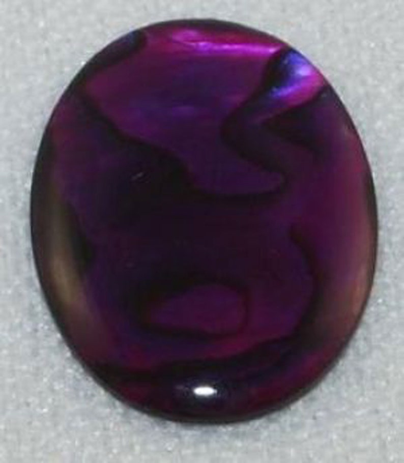 May include: A purple abalone shell cabochon with iridescent swirls. The shell is oval shaped and has a smooth, polished surface.