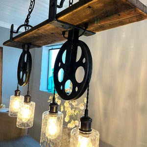 May include: A rustic wooden shelf with black metal pulley wheels and hanging light fixtures. The lights have clear glass shades and Edison bulbs.