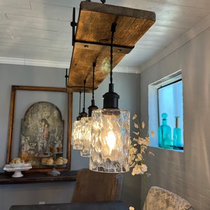 May include: A rustic wooden light fixture with four clear glass pendant lights hanging from black cords. The fixture is mounted to the ceiling and has a distressed wood finish. The lights are on and casting a warm glow.