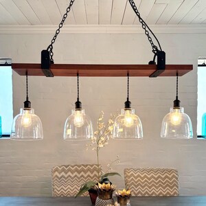 May include: A rustic, four-light pendant light fixture with clear glass shades and Edison-style bulbs. The fixture is suspended from a dark wood beam and black chains. Decorative turquoise glass bottles are visible in the background.