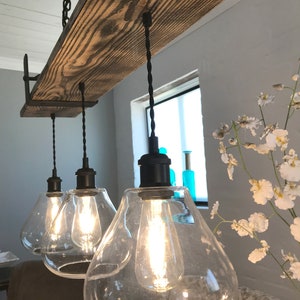 May include: A rustic wooden beam chandelier with three clear glass globe light fixtures and black cords hanging from the ceiling.