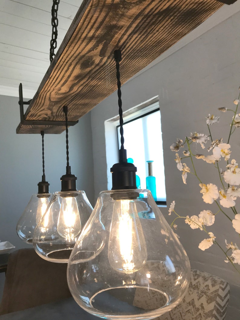 May include: A rustic wooden beam chandelier with three clear glass globe light fixtures and black cords hanging from the ceiling.
