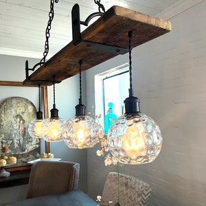 May include: A rustic wooden beam chandelier with four clear glass globe light fixtures. The chandelier is hanging from a chain and has black metal accents.