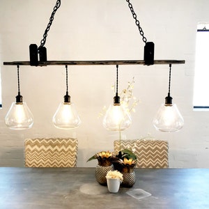 May include: A rustic wooden chandelier with four clear glass globe light fixtures hanging from black chains. The chandelier is suspended over a dining table with two chairs and a centerpiece of gold pineapple-shaped vases.