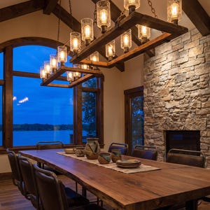 May include: A rectangular wooden chandelier with twelve glass cylinder shades and Edison-style bulbs, suspended by chains above a long live-edge wooden dining table with dark leather chairs and ceramic pottery pieces arranged on a runner.