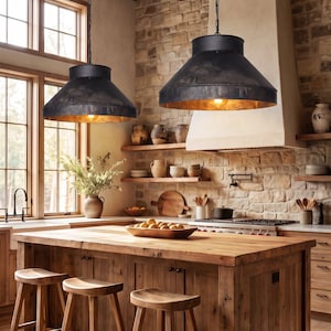 May include: Two large, matte black metal pendant lights with wide, conical shades and warm, glowing bulbs suspended by black chains above a wooden kitchen island featuring three matching wooden stools with contoured seats and four legs.