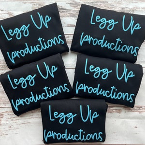 May include: Five black t-shirts with the text "Legg Up Productions" in light blue lettering.