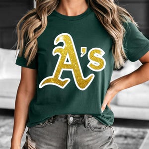 May include: A green t-shirt with a gold glitter "A's" graphic.