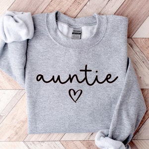 May include: Gray sweatshirt with the word "auntie" in black cursive lettering and a small black heart below it.