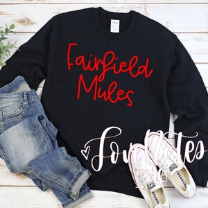 May include: Black crew neck sweatshirt with the words "Fairfield Mules" in red script. Below, the word "Love" is written in white script, followed by "mates". The sweatshirt is paired with blue jeans and white sneakers.
