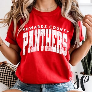 Puede incluir: Una camiseta roja con la inscripción "EDWARDS COUNTY PANTHERS" en letras blancas desgastadas. La camiseta tiene mangas cortas y cuello redondo. El texto está centrado en la parte delantera de la camiseta.