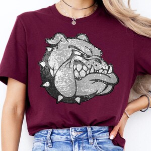 May include: A maroon t-shirt with a silver sequined bulldog graphic. The bulldog is facing right and has a fierce expression.