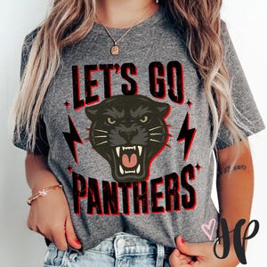 Puede incluir: Camiseta gris con el texto "LET'S GO PANTHERS" en negro y rojo. La camiseta presenta un gráfico de cabeza de pantera negra con acentos de rayos. Un diseño casual y deportivo.