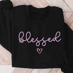 May include: Black sweatshirt with a pink cursive "blessed" and a small pink heart.