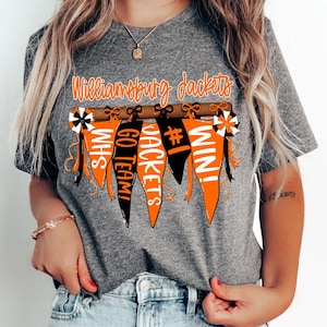 May include: Gray t-shirt with the text "Williamsburg Jackets" and a graphic of orange and black pennants with the text "WHS", "GO TEAM!", "JACKETS", "#1", and "WIN!"