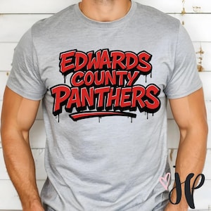 Puede incluir: Camiseta gris claro con la inscripción "EDWARDS COUNTY PANTHERS" en rojo, contorneada en negro con efecto de pintura goteando. La camiseta es de cuello redondo.