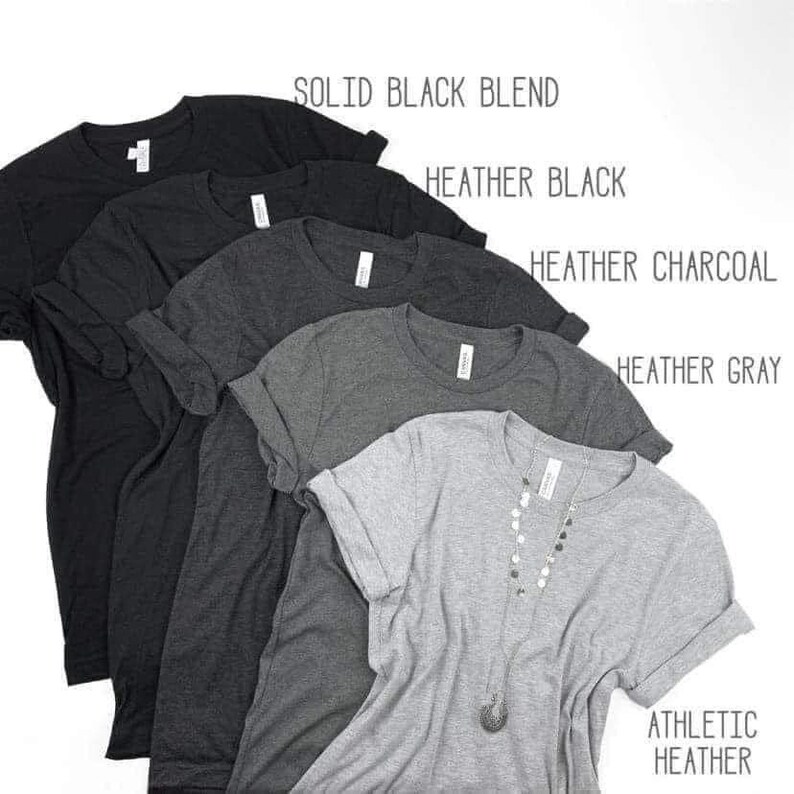 May include: Five t-shirts in different colors, from left to right: solid black blend, heather black, heather charcoal, heather gray, and athletic heather. The t-shirts are folded and stacked on top of each other.