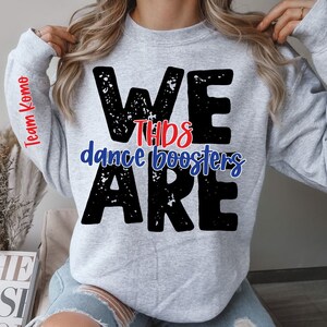 May include: Gray sweatshirt with the text "WE ARE THE DANCE BOOSTERS" in black with a distressed look. The text "THE" is in red. The left sleeve has the text "Team Komo" in red.