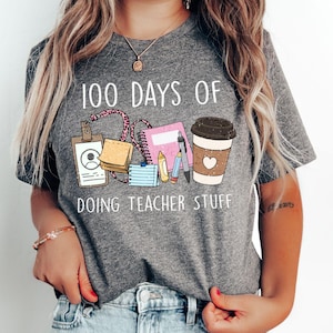 May include: Gray t-shirt with the text "100 Days of Doing Teacher Stuff" and a graphic of school supplies, including a coffee cup, pencils, and a notebook.