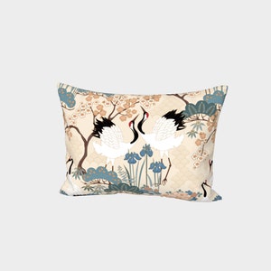 May include: A cream-colored pillow with a Japanese-inspired design featuring two white cranes with black wings and red beaks, surrounded by blue and green floral patterns and gold accents.