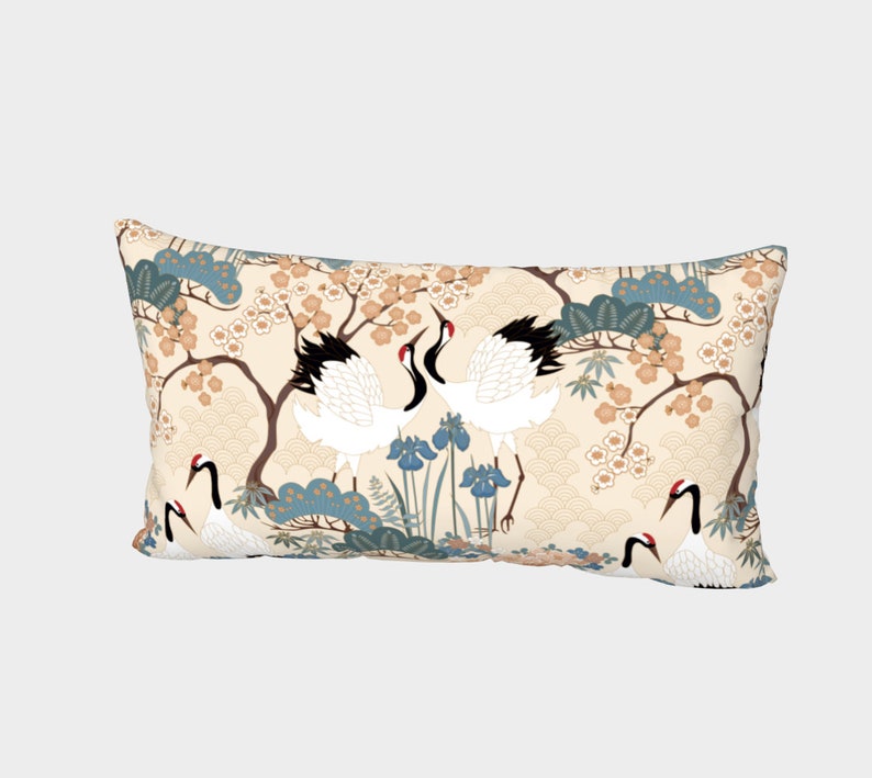May include: A rectangular throw pillow with a cream background and a repeating pattern of white cranes, blue and green trees, and pink flowers.