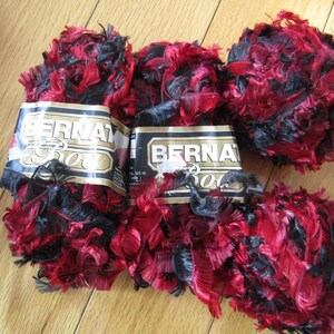 May include: Several skeins of Bernat Boa yarn in red and black. The yarn is fluffy and textured, with a mix of red and black fibers. The labels are visible, indicating the brand and type of yarn.