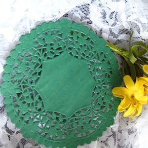 May include: A green paper doily with a scalloped edge and a floral cut-out design. The doily has a solid green center and is decorated with a yellow flower and green stem.