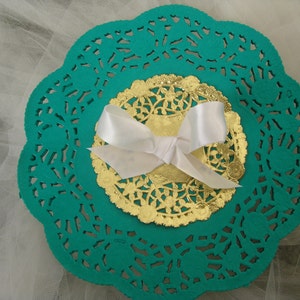 May include: A teal doily with a gold doily and a white bow in the center.