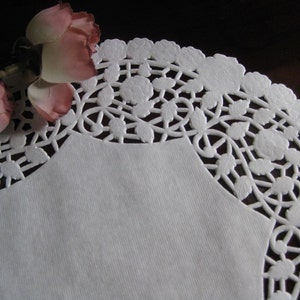 May include: White paper doily with a delicate floral design. The doily has a scalloped edge and is perfect for adding a touch of elegance to any occasion.