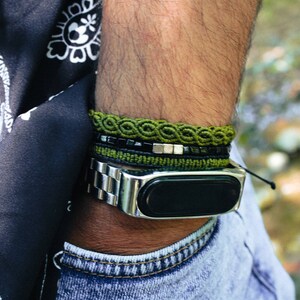 May include: A person wearing a black and white paisley patterned shirt with a green, black and silver bracelet and a black fitness tracker with a silver band.