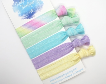 May include: Set of six pastel tie dye hair scrunchies. The scrunchies are made of soft, stretchy fabric and have a subtle shimmer. The colors are a light pink, green, blue, purple, and yellow.