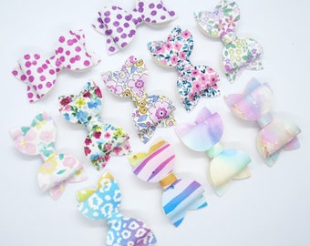 May include: A collection of ten colourful hair bows with various patterns, including polka dots, floral prints, and abstract designs. The bows are made of fabric and are perfect for adding a touch of whimsy to any hairstyle.