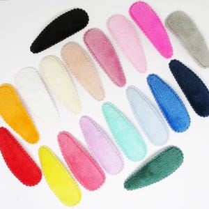 May include: Assortment of 18 fuzzy hair clips in various colours, including pink, blue, green, yellow, orange, red, white, and black. The clips are oval shaped and have a scalloped edge.
