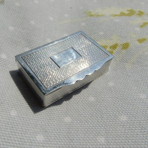 Puede incluir: Una caja rectangular de plata con una superficie texturizada y un panel rectangular elevado en la parte superior.