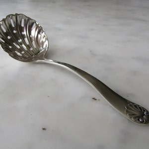 May include: A silver sugar spoon with a decorative shell design and a perforated bowl.