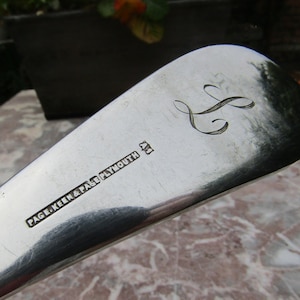 May include: Close-up of a silver spoon with the inscription "PAGE, KEEN & PAGE, PLYMOUTH" and a cursive letter "S" engraved on the handle.
